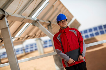 Asian male workers in blue helmets and red overalls hold laptops in the solar photovoltaic zone
