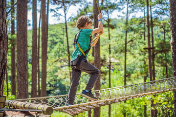 Portrait of cute little boy walk on a rope bridge in an adventure rope park