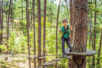 Portrait of cute little boy walk on a rope bridge in an adventure rope park