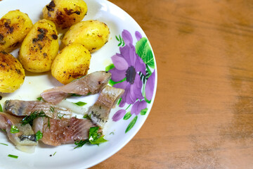 Sliced herring fillet with fried potatoes on a white plate. Home table with space for copy and paste