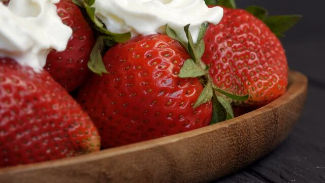 Juicy ripe big red strawberries on an eco bamboo plate on top with whipped cream cloes up view.
