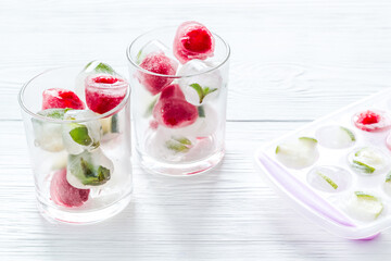 Cocktail glasses with berries in ice cubes on white table