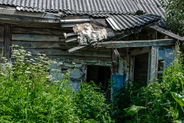 Entrance to an old village house with a collapsed roof and walls, among tall grass.