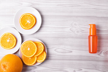 vitamin c concept in beauty industry products represented by an orange plastic bottle of lotion, cream, fluid or spray and a group of orange citruses