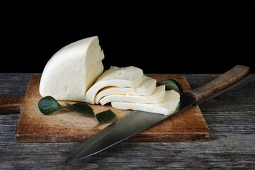 Sliced cheese and knife on the old wooden board with black background