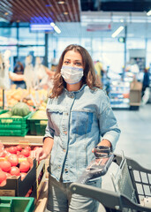 Beautiful girl in a mask on her face in a supermarket makes purchases

