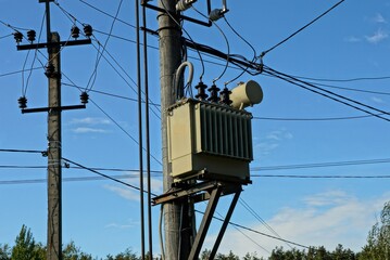 gray iron transformer on a concrete pole with electric wires against a blue sky