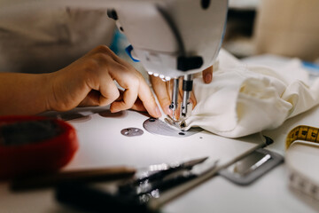 Close up of a tailor working at a sewing machine, soft focus on needle and fingers.