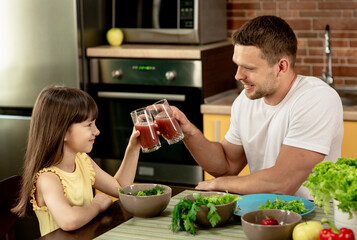 Cheerful father and his daughter having breakfast together in the kitchen, talking, holding glasses...