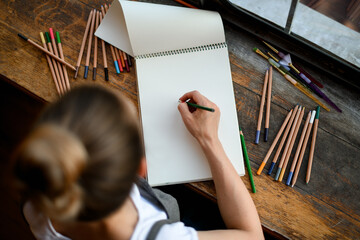 top view on sketchbook on wooden table in which young woman draws