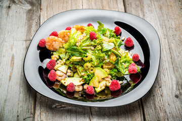 Salad with shrimps, avocado and fresh raspberries, on a black plate.