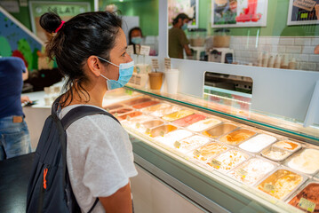 Fototapeta na wymiar young woman with face mask buying ice cream in ice cream shop, an example of daily life during the corona virus pandemic