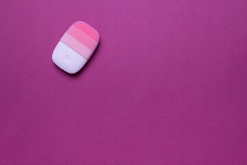 pink electric face massager on purple background, top view with copy space