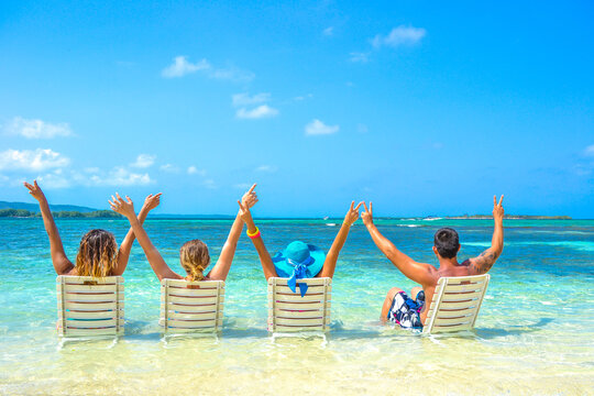 group of young friends on caribbean pristine beach with arms up, enjoying and sharing summer holidays, boys and girls celebrating life together