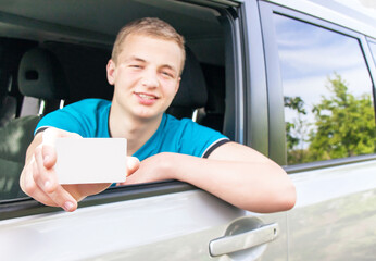 Car driver. Caucasian teen boy showing an empty white card in the new car.