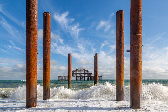 Waves crashing in front of the ruins of the West Pier in Brighton, with a blue sky overhead