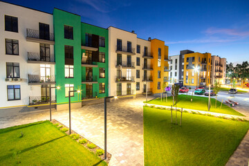 Yard between residential apartment buildings with green grass lawns and modern flat housing. Real estate development.