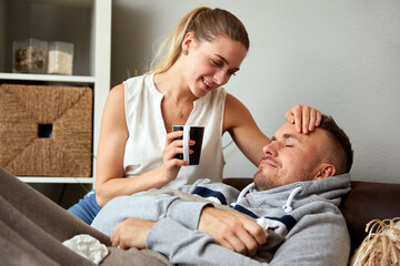Smiling Young Woman Sitting By Unwell Boyfriend