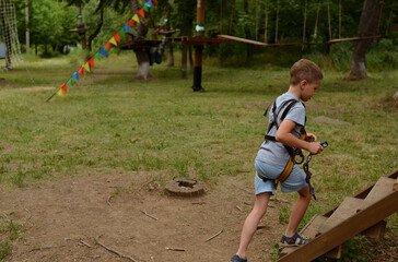 A child in equipment for climbers. A boy in the park walks over obstacles.