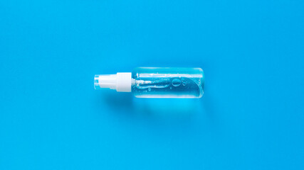 Hand sanitizer transparent bottle with spray cap at the middle of blue background. Simple flat lay with pastel paper texture. Medical concept. Stock photo.