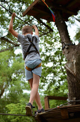 
A child in equipment for climbers. A boy in an amusement park walks a tightrope with obstacles.