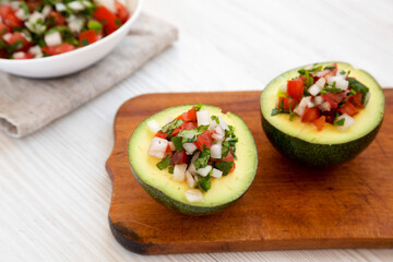 Homemade Pico de Gallo Stuffed Avocado on a rustic wooden board on a white wooden table, side view.