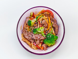 Udon noodles with meat in a plate on a white surface. With vegetables greens