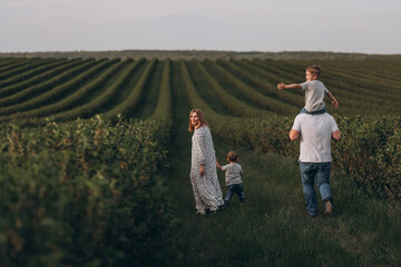 Big young happy family in the field on the nature. Mom, dad and 2 sons are having fun, running, fooling around together. Happiness and smiles around