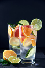 Health care, fitness, healthy nutrition diet concept. Fresh cool homemade citrus infused detox water with grapefruit, orange, lemon and lime and ice in glasses on dark background.