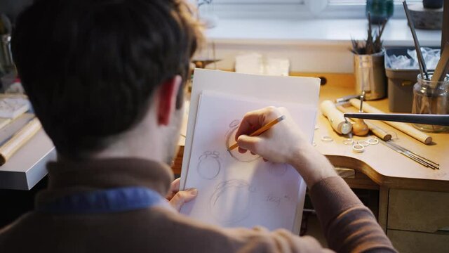 Over the shoulder view of male jeweller sketching out design for ring in studio - shot in slow motion 