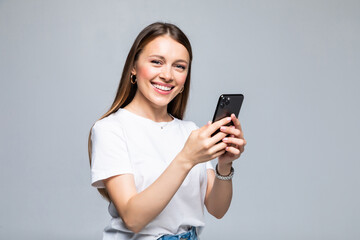 Fototapeta premium Young Woman smiling and texting on her mobile phone, isolated over white background.