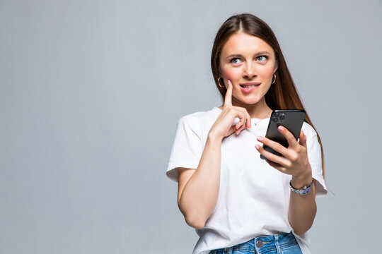 Portrait Of A Thoughtful Doubtful Asian Woman Talking On Mobile Phone And Looking Up Over White Background