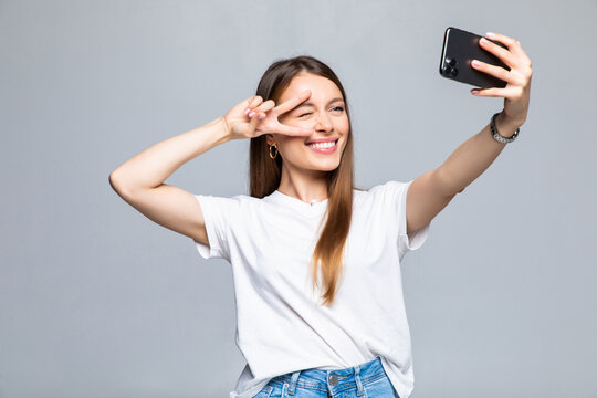 Portrait of a young attractive woman making selfie photo on smartphone on a white background