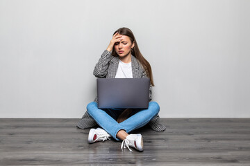 Young woman with a laptop sitting on the floor with tired and bored expression