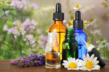 Obraz na płótnie Canvas Bottles of essential oils and wildflowers on wooden table against blurred background