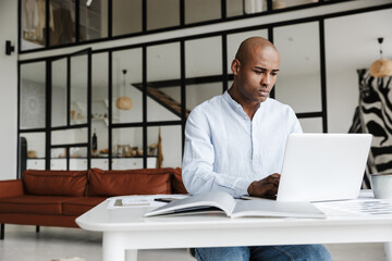 Photo of serious man working with laptop while sitting at table