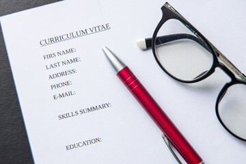 Curriculum Vitae form to be filled in, with pen and glasses next to it. Draftimg the CV. Filling the form. 