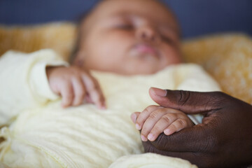 Close-up of African man holding little hand of newborn while he sleeping in the bed