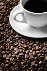 Cup of coffee drink sitting on a bed of roasted coffee beans background. Close up of a brown surface texture of aroma black caffeine drink ingredient for coffee beverage.