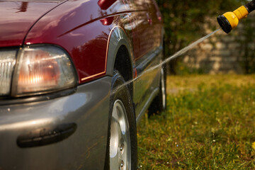 A man washes a car from a hose. Car wash.