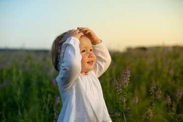 A girl standing in a field of flowers is illuminated by the sun. The little girl smiles