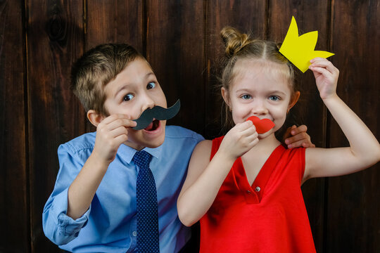 A kid with props for a photo booth. Children with the requisite mustache on wooden background. Event, holiday, party.