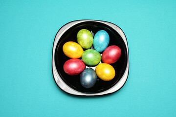 many colors eggs on black plate isolated on aquamarine background