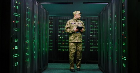 Caucasian military male officer coming in the server room with tablet device in hands, working with secret data and anti-terrorism information. Cybersecurity concept.