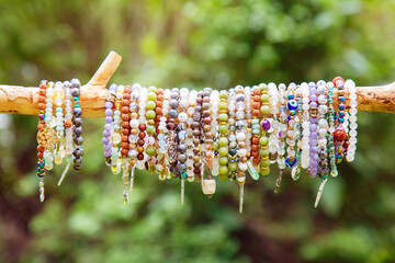 Collection of crystals mineral stone beads yoga bracelets hanging on the branch on natural green bokeh background