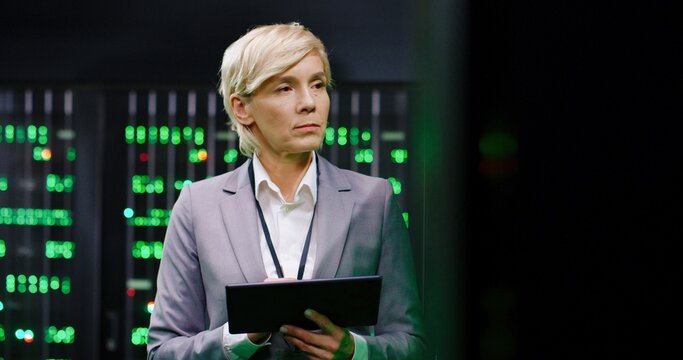 Caucasian female system admonistrator tapping on tablet device while working with secret data at server room. Governmental analytic center. Woman operating with information. Telecommunication.