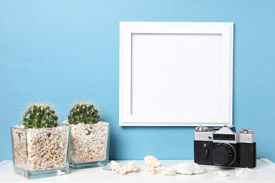 white blank frame, plant cactus with shells on white table against the blue wall. Mockup with copy space