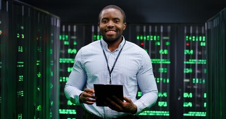 Portrait of young handsome African American man smiling cheerfully too camera in database center...