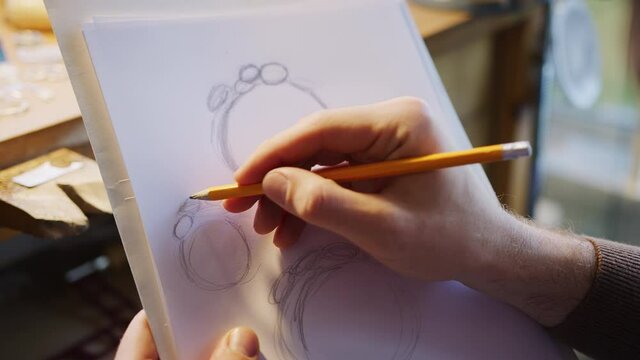 Close up of male jeweller sketching out design for ring in studio - shot in slow motion 