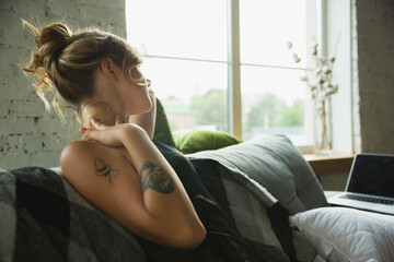 Setting hair into bun, looks cozy. Portrait of young girl in modern apartment in the morning. Resting, calm, salisfied. Youth, wellness concept. Elegance woman in silk dress spending time comfortable.